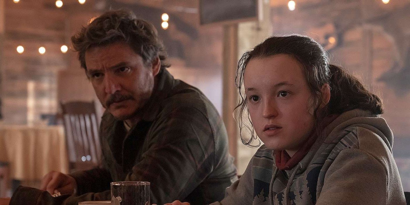 Pedro Pascal as Joel and Bella Ramsey as Ellie at a bar looking in the same direction in The Last of Us Season 1.