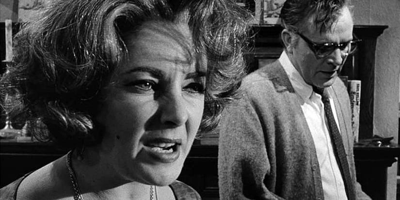 A close up of Elizabeth Taylor with Richard Burton in the background