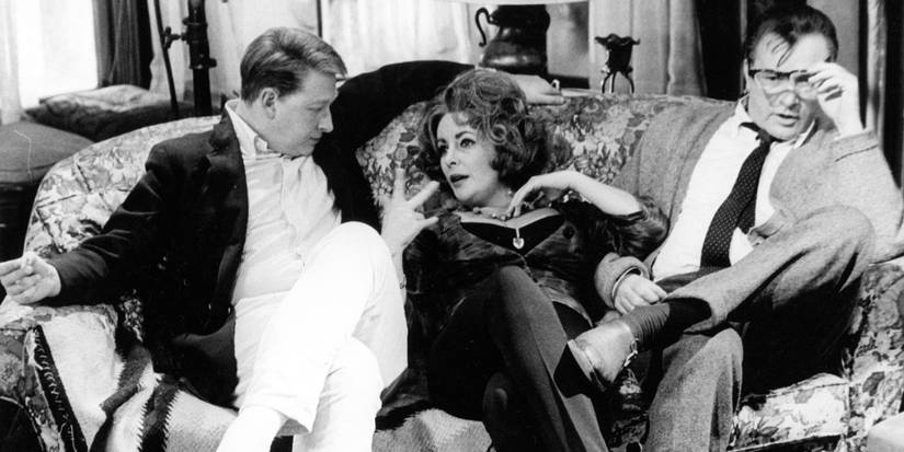 Elizabeth Taylor sitting on a sofa between Richard Burton and George Segal in Who's Afraid of Virginia Woolf?
