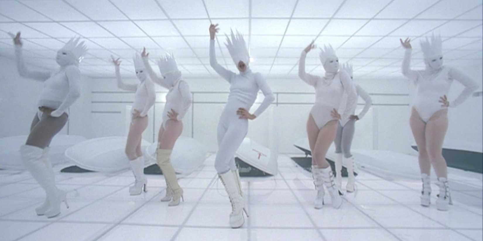 Lady Gaga and dancers in all white outfits with tall, pointy hats in the music video for Bad Romance.