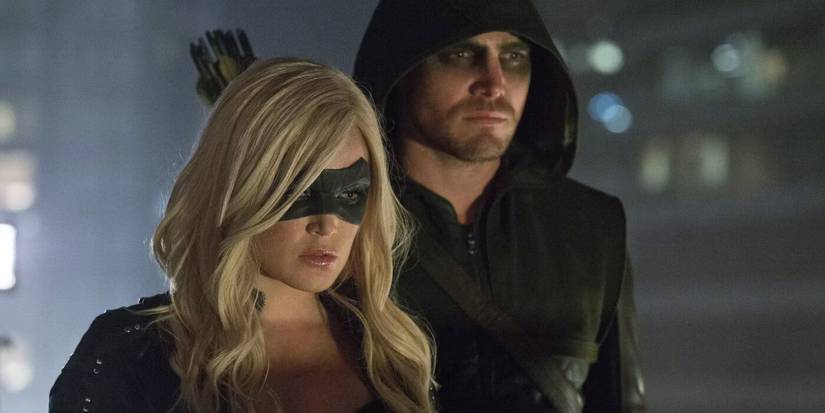 Sara Lance as the Black Canary and Oliver Queen as Arrow look down at something, frowning, on Arrow