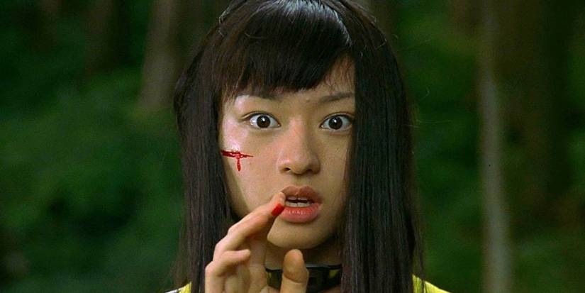 A girl with blood on her face trying to touch something in front of her with a bloody finger