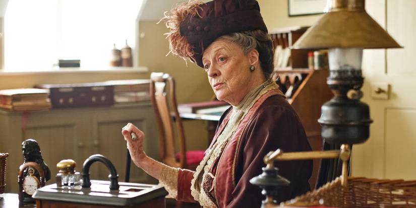 Maggie Smith as Violet Crawley sits and looks to the side, holding something in her hand in Downton Abbey.