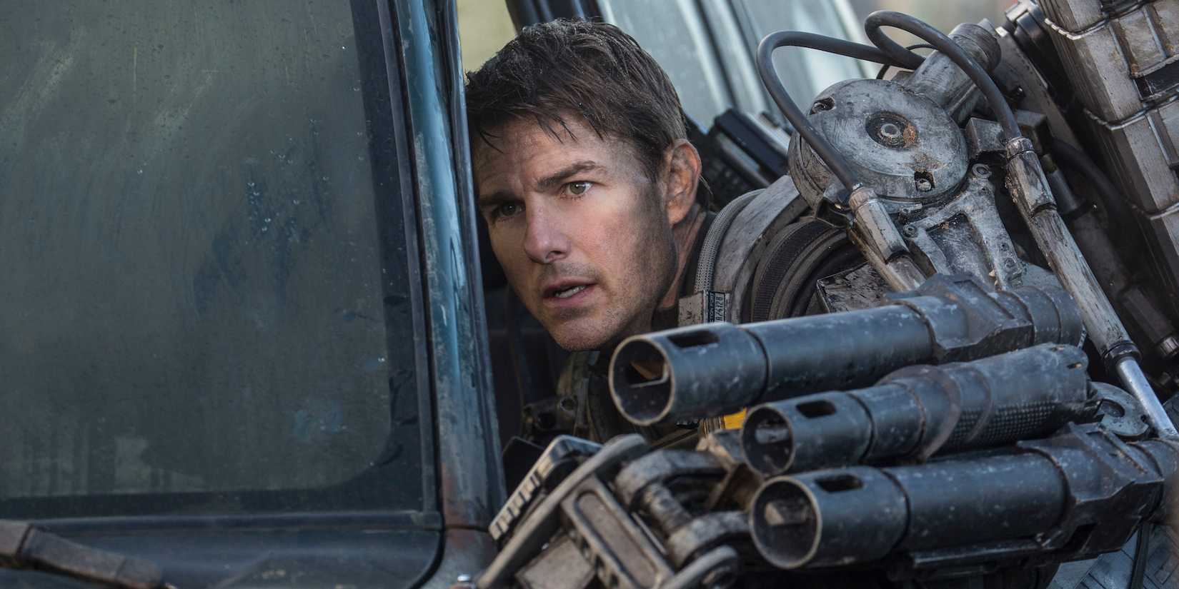 Tom Cruise as Cage wearing a mech-suit and hiding behind a car in Edge of Tomorrow