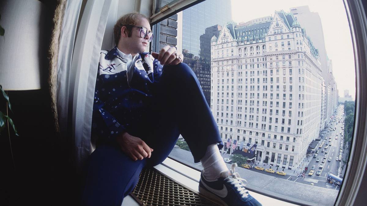 Young Elton John sitting on a window sill looking out at a city