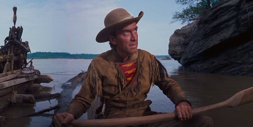 Linus Rawlings (Jimmy Stewart) sits by a lake holding an oar as a raft floats behind him in 'How the West Was Won' (1962).
