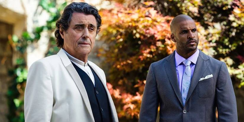 Ian McShane (Wednesday) and Ricky Whittle (Shadow) looking to the side in American Gods.