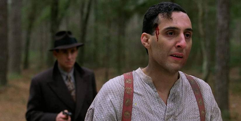 John Turturro with blood on his forehead and a man holding a weapon behind him in Miller's Crossing.