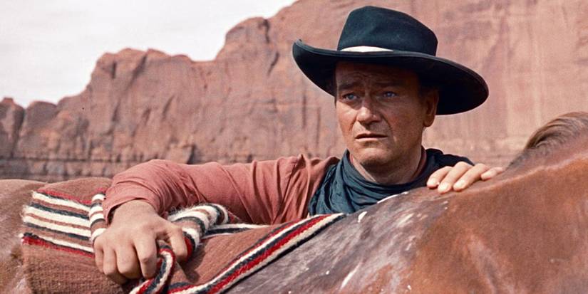 John Wayne as Ethan Edwards in The Searchers, standing next to a horse and looking perplexed.