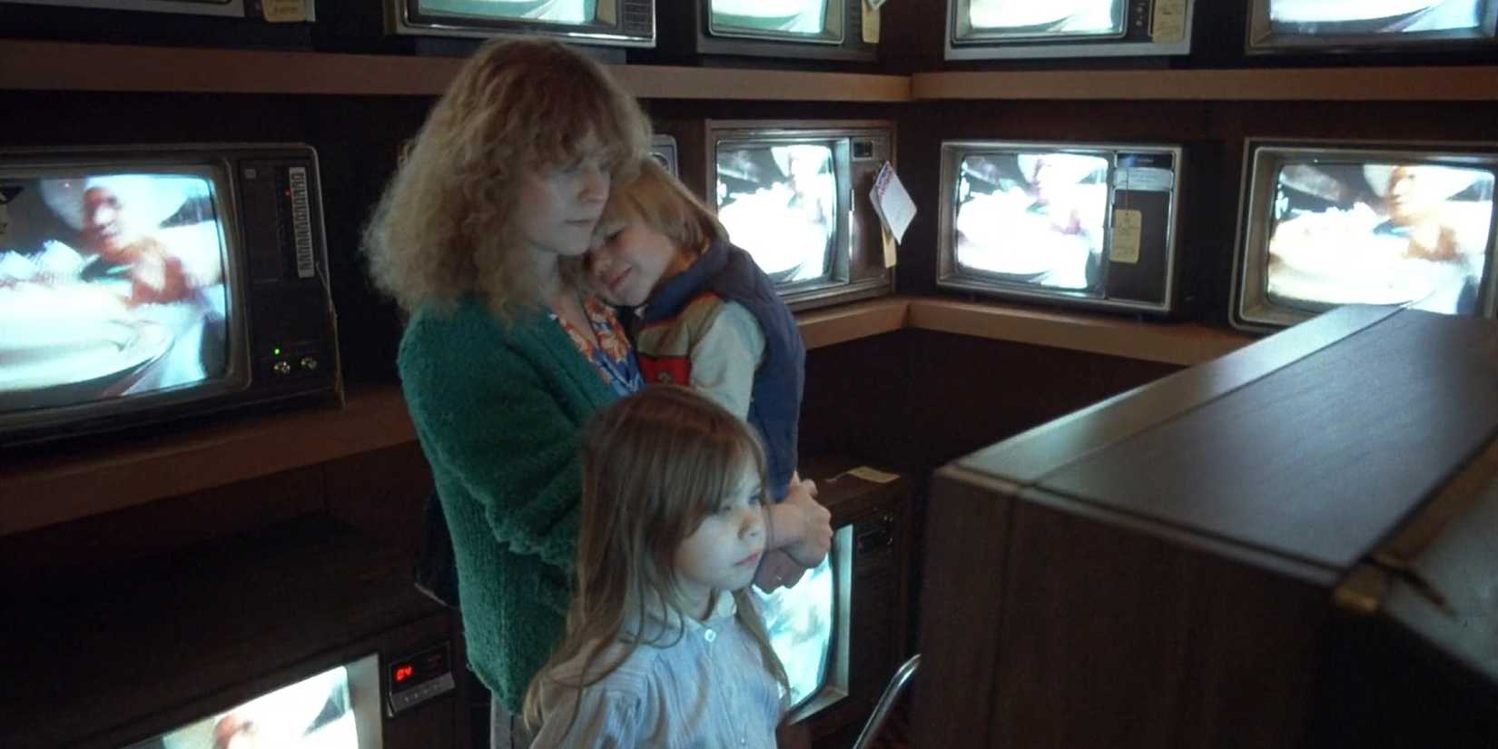 A woman and two children in a room full of TVs