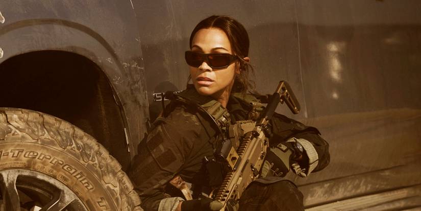 Zoe Saldana as Joe in military gear and sunglasses behind the wheel well of a truck in Lioness Season 2.