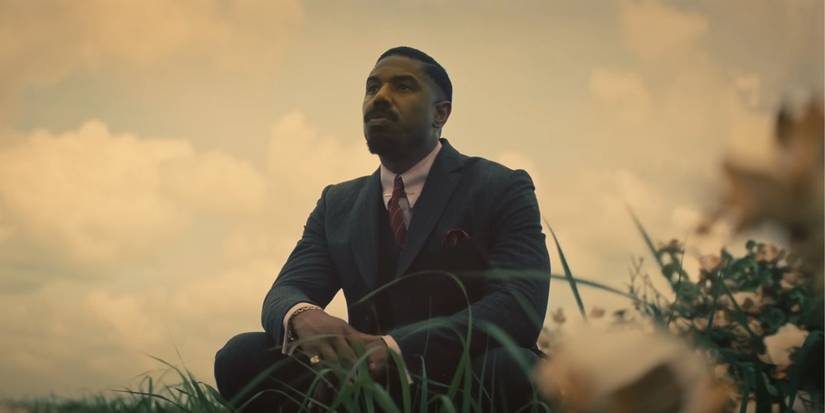 Michael B Jordan in a suit crouching in a meadow in Sinners
