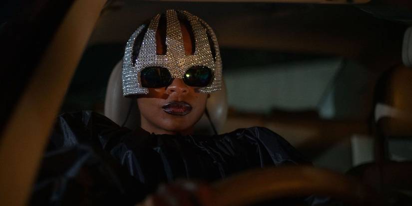 Susan Chardy as Shula wearing a beanie with sunglasses.