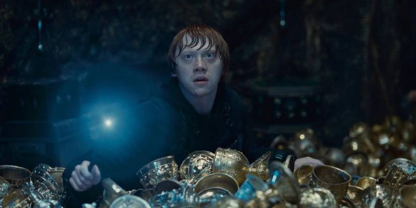 Ron Weasley hold his lit wand amidst a pile of treasure in 'Harry Potter and the Deathly Hallows: Part 2'