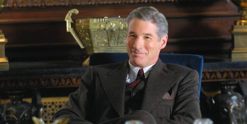 Richard Gere as Billy Flynn smiling at his desk in 