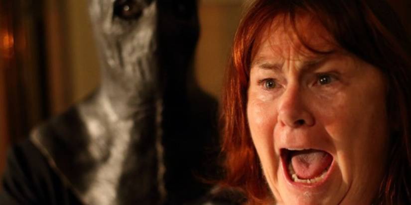 A woman screams in terror as a figure with a horror mask stands behind her in Slasher.