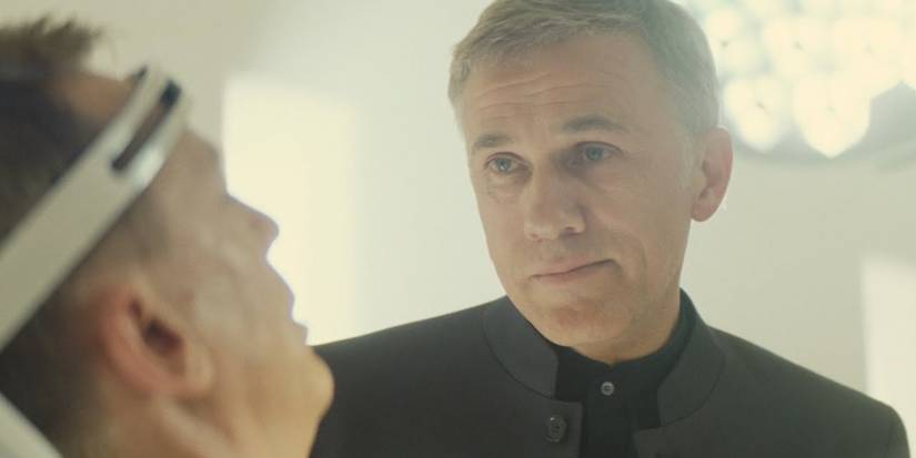 Blofeld (Christoph Waltz) stands over a restrained James Bond, looking him in the eye in Spectre.