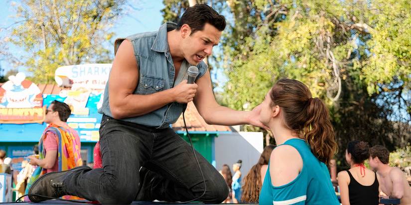 سكايلر أستين في دور جريج يقف على طاولة في الحديقة ويغني لراشيل بلوم في فيلم Crazy Ex-Girlfriend.