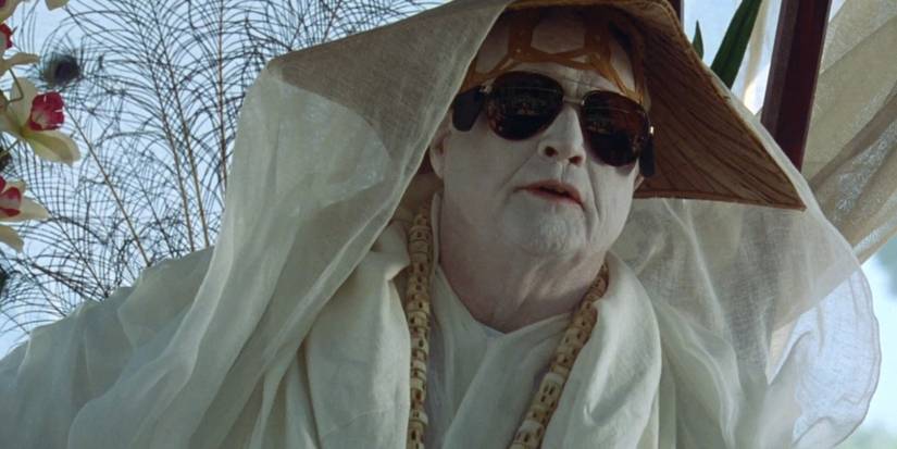 Dr Moreau, played by actor Marlon Brando, wears a white ceremonial robe with matching face paint and sunglasses, in The Island of Dr. Moreau