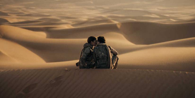 Paul Atreides (Thomthée Chalemet) and Chani (Zendaya) share a kiss as they sit atop a sand dune overlooking the vast desert landscape of Arrakis in "Dune Part Two" (2024).