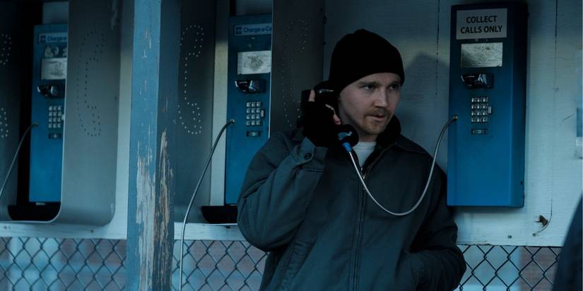 Paul Dano in a hat, hoodie, and gloves talks on a pay phone in 'Escape at Dannemora.'
