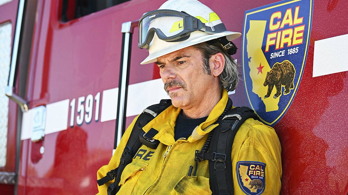 Billy Burke as Vince Leone leaning against a Cal Fire engine in his firefighter gear in Fire Country