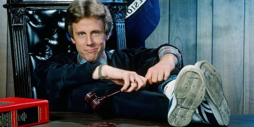 Harry Anderson as Judge Harry Stone sitting with his sneakered feet up on the bench looking at the camera in Night Court (1984-92).