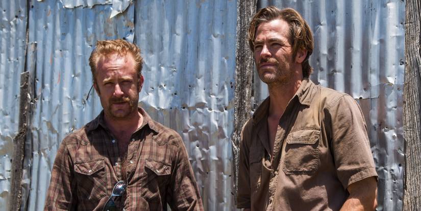 Ben Foster's Tanner standing with Chris Pine's Toby look at something off-screen in Hell or High Water.