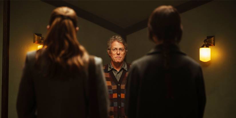 A sinister shot of Mr Reed, played by actor Hugh Grant framed between Sisters Barnes and Paxton, played by actors Chloe East and Sophie Thatcher, with their backs to the camera in Heretic