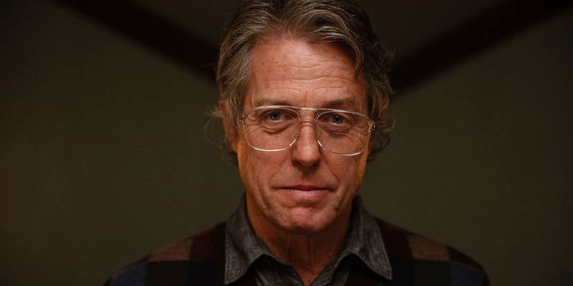 Close-up of Hugh Grant as Mr. Reed in glasses smiling down towards the camera eerily in Heretic
