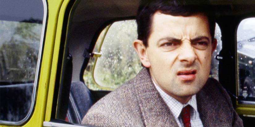 Rowan Atkinson as Mr. Bean squinting out the window of a yellow car in 'Mr. Bean' (1990-1995).