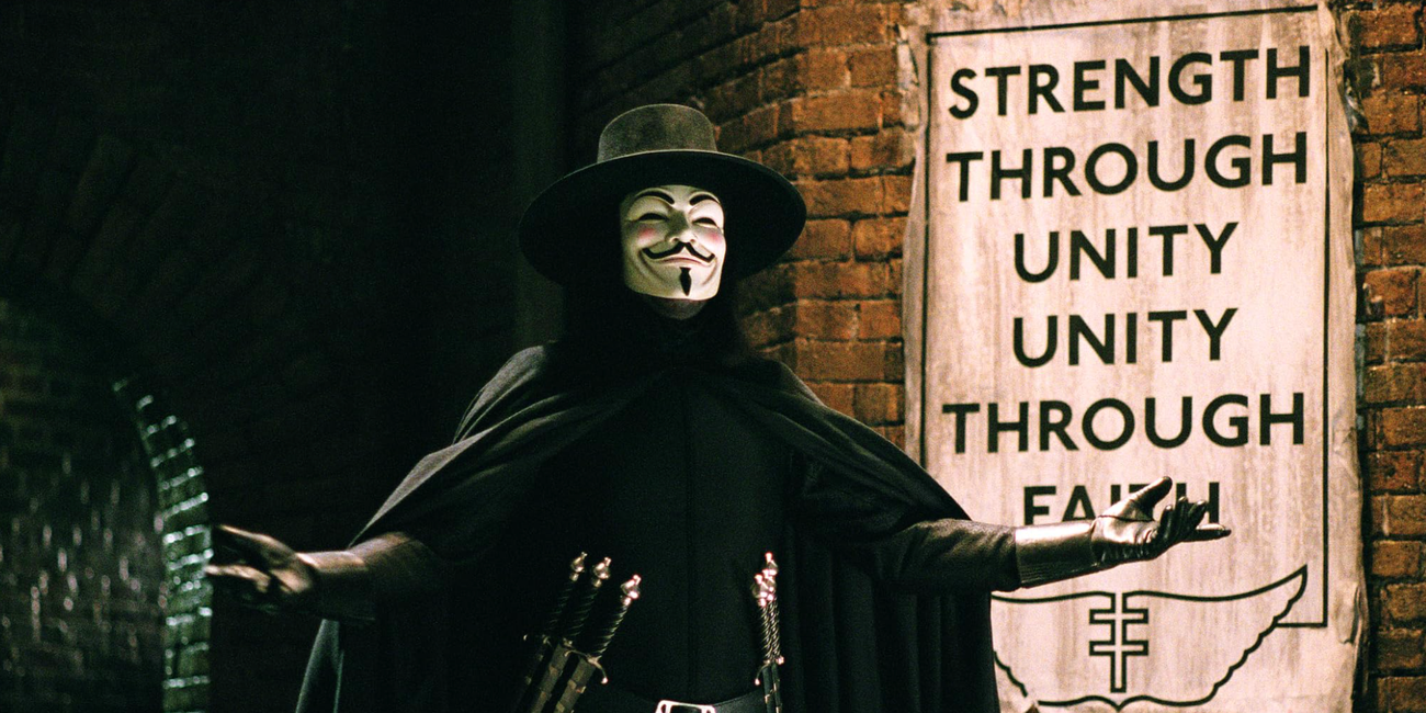 V stands with arms open in front of a sign reading "Strength Through Unity; Unity Through Faith"