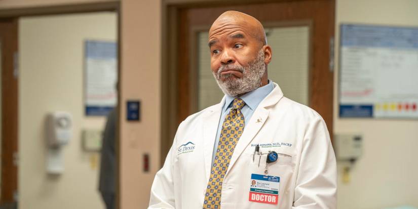Ron (David Alan Grier) in a doctor's labcoat and half-smiling at something offscreen in St. Denis Medical