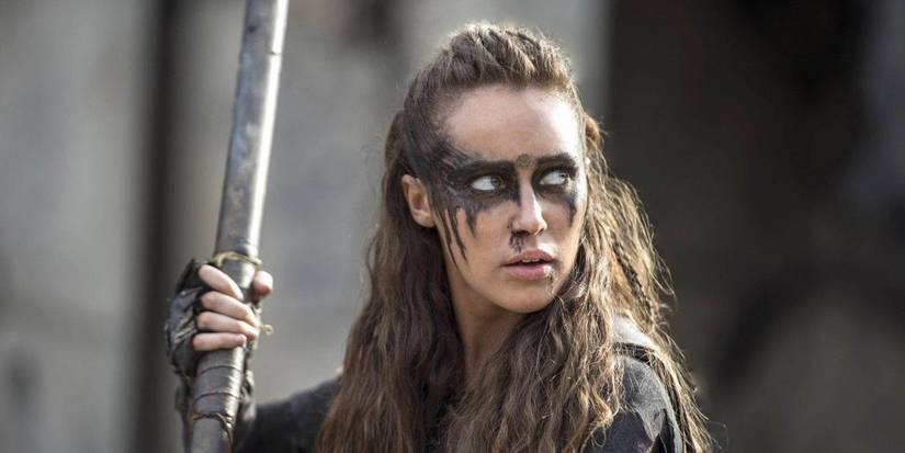 Alycia Debnam-Carey as Lexa holding a long weapon with face paint in The 100. 