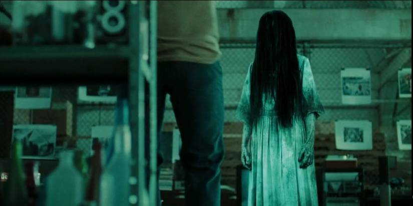 Daveigh Chase as Samara, standing in a white dress with long black hair covering her face in The Ring.