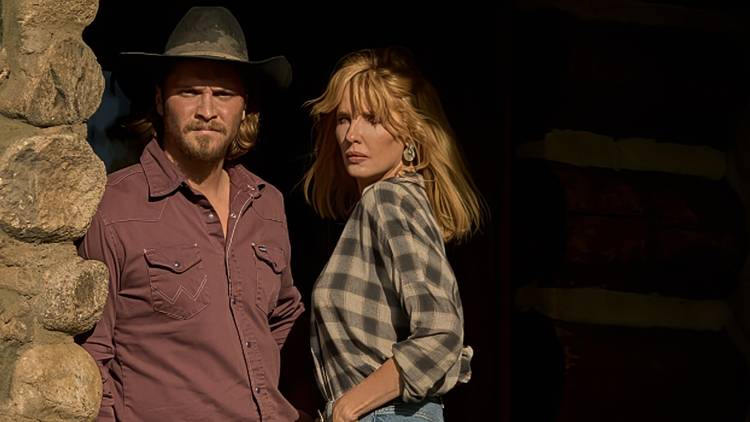 Luke Grimes as Kayce Dutton and Kelly Reilly as Beth Dutton standing on the front porch of the ranch in Yellowstone Season 5