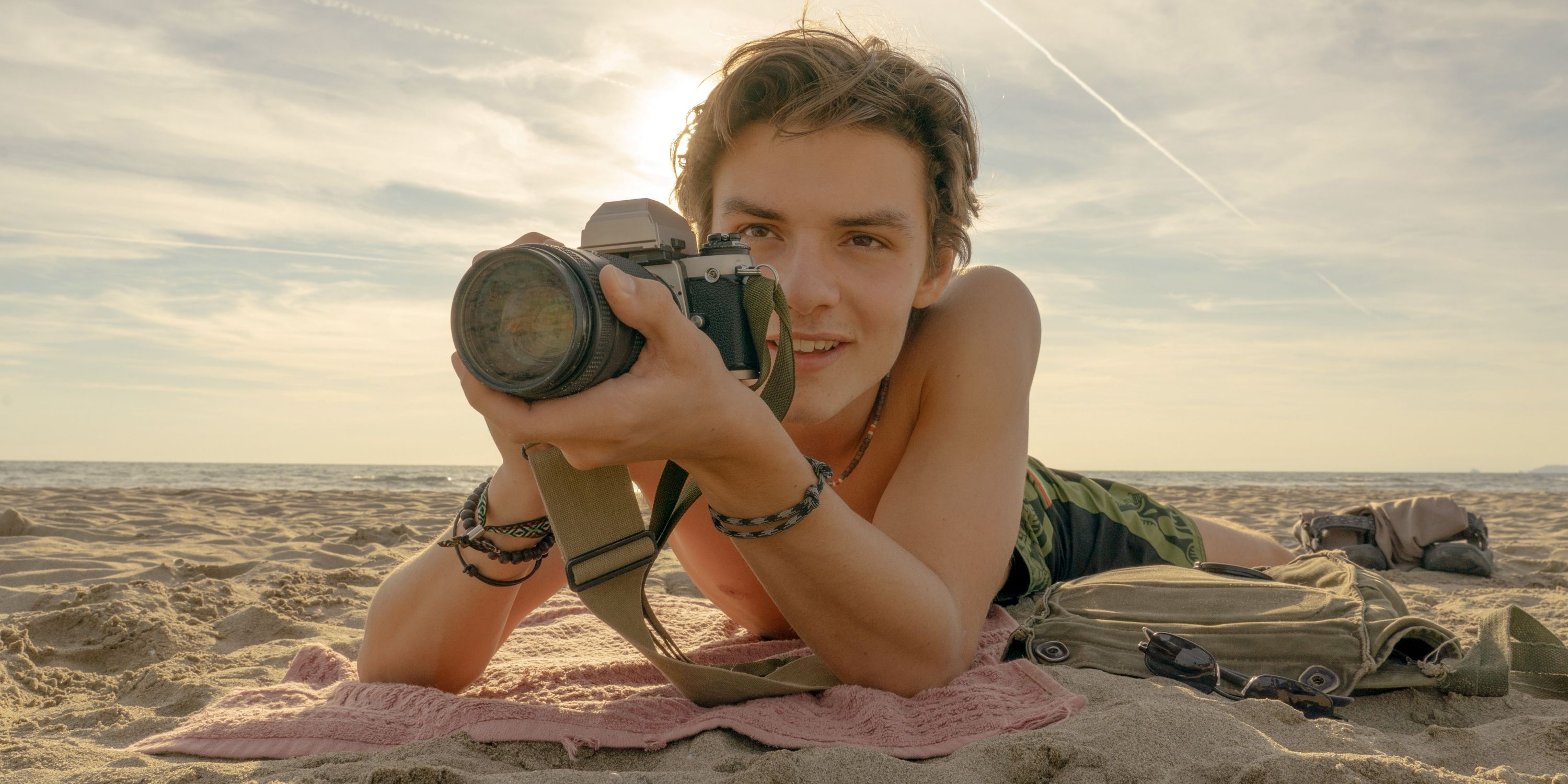 Louis Partridge as Jonathan holding his camera up to his eye on the beach in Rome in Disclaimer