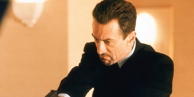 Robert De Niro aiming a gun at something toward the ground in Heat