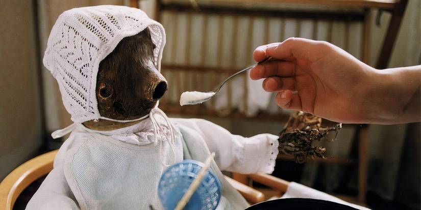 A person spoon-feeding a strange-looking wooden puppet thing in the horror movie Little Otik (2000)
