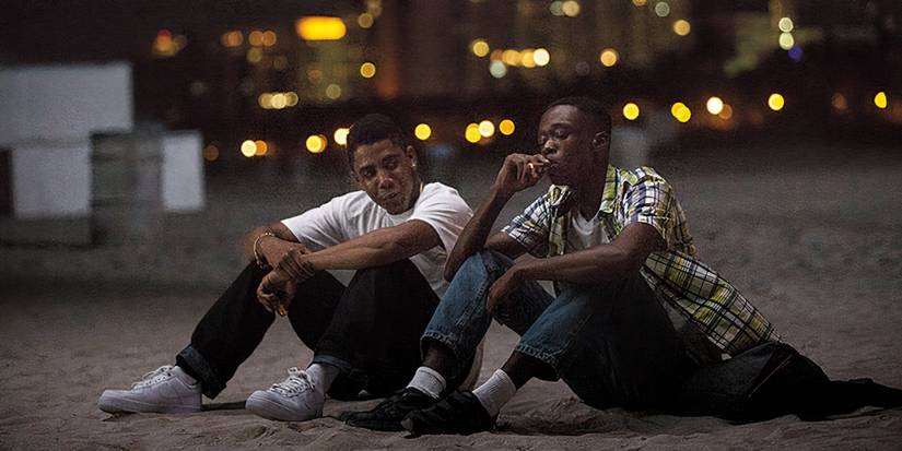 Two teenagers sit together with a city in the background in Moonlight.