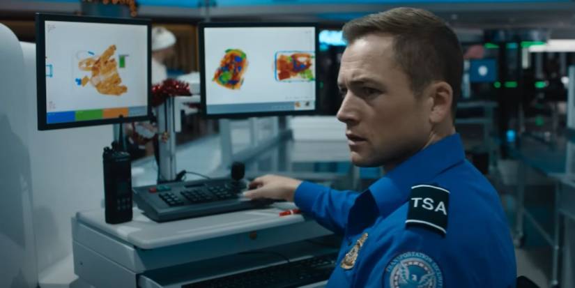 Taron Edgerton melihat monitor keamanan bandara di 'Carry-On'.