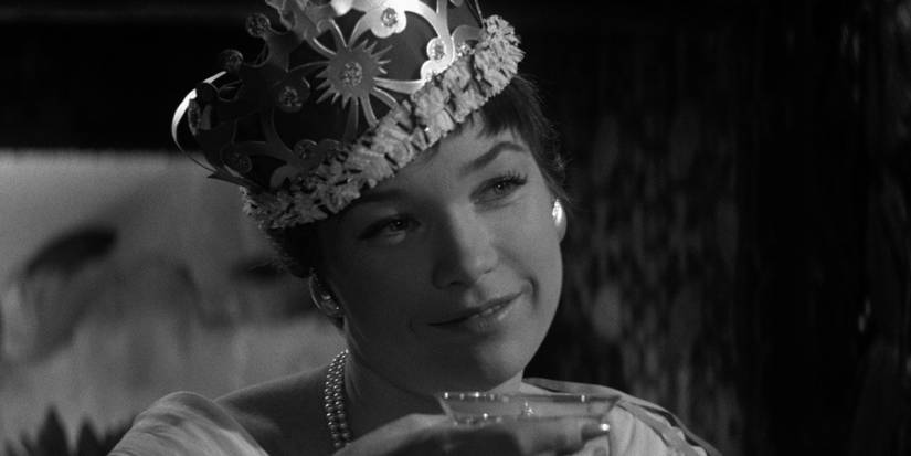 Fran Kubelik, played by Shirley MacLaine, holds up a glass while wearing a crown in 'The Apartment'.