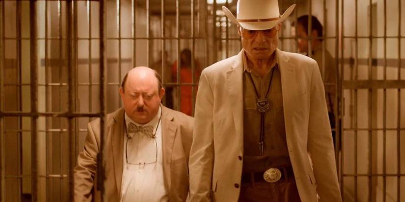 Two of the main characters walk down a prison hallway with bars and inmates in The Human Centipede 3.