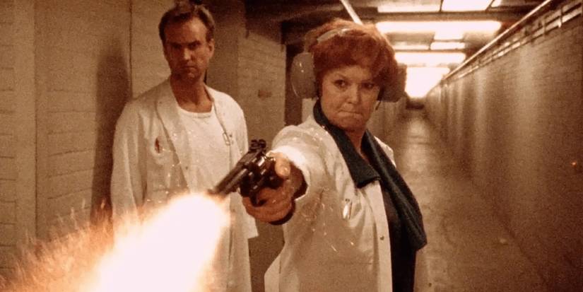 Uma mulher usando proteção auricular dispara uma arma enquanto um homem assiste em 'O Reino'