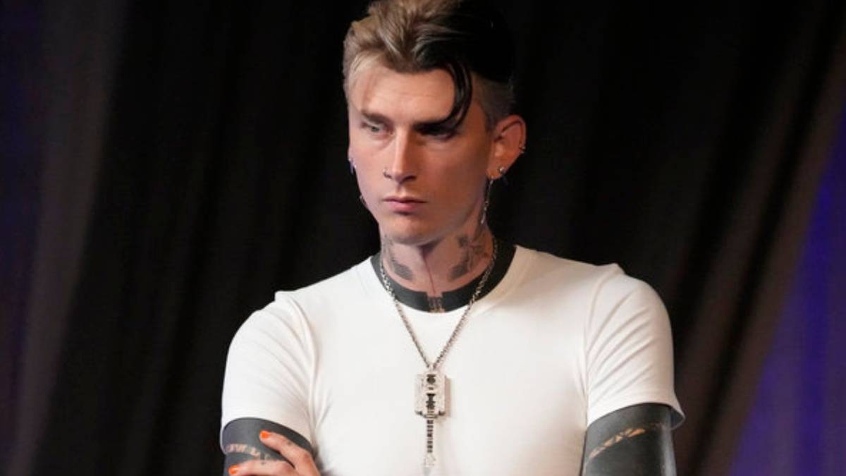 Machine Gun Kelly has his arms crossed as he listens to Team Gwen singers on 'The Voice' Season 26.