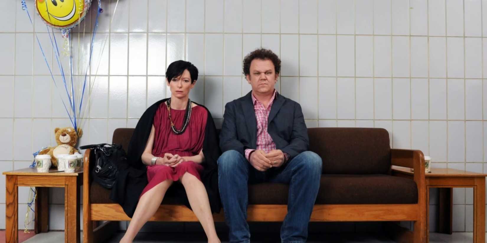 Eva and Franklin sitting on a bench looking numb in We Need to Talk About Kevin.