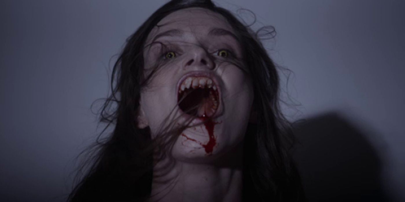 Sarah, played by actor Alexandra Essoe, with yellow eyes, fangs and blood pouring from her mouth in Starry Eyes