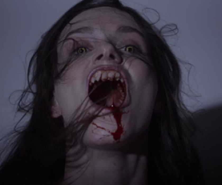 Sarah, played by actor Alexandra Essoe, with yellow eyes, fangs and blood pouring from her mouth in Starry Eyes