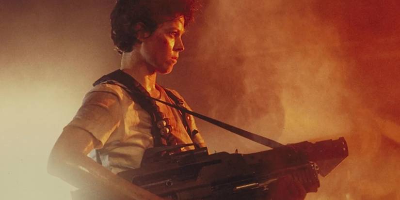 Ellen Ripley (Sigourney Weaver) stands holding a machine gun as orange light shines through smoke in 'Aliens' (1986).Alien