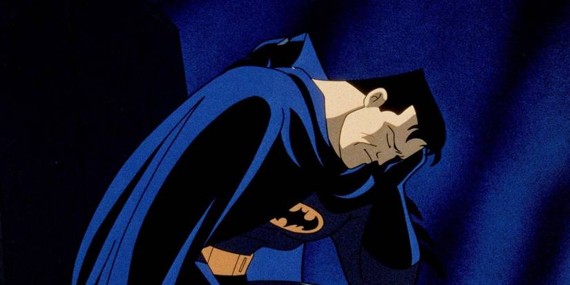 Batman sits with his head in his hand and his mask off, looking sad in Batman: Mask of the Phantasm